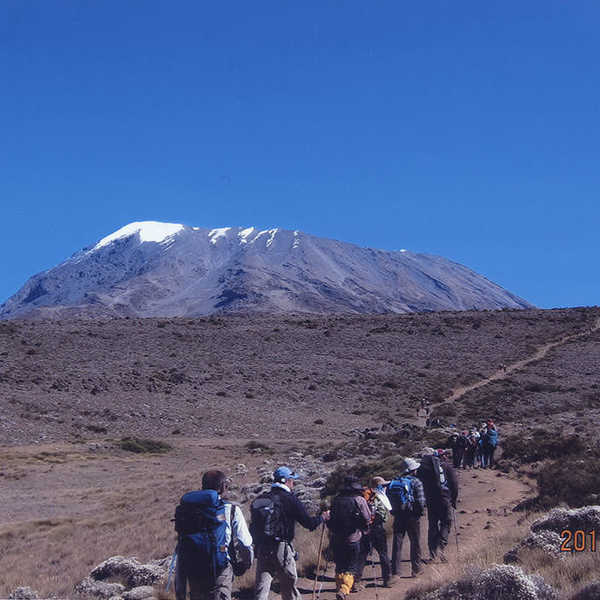 投稿写真／入山3日目のホロンボハットからキボハットに向かうメンバー。山道の先にどっしりと鎮座するキリマンジャロ山。